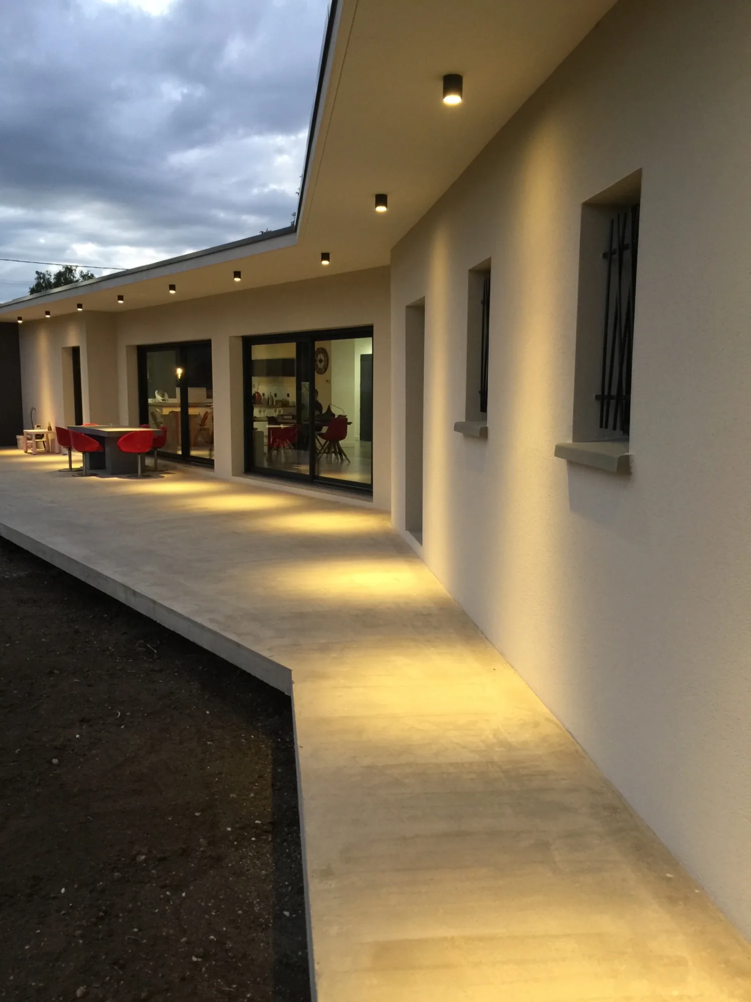Terrasse couverte éclairée le long d'une maison neuve, à la tombée du jour