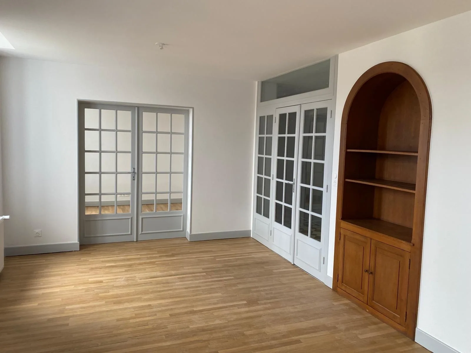 Pièce de vie rénovée : parquet, portes vitrées à petits carreaux et bibliothèque cintrée en bois