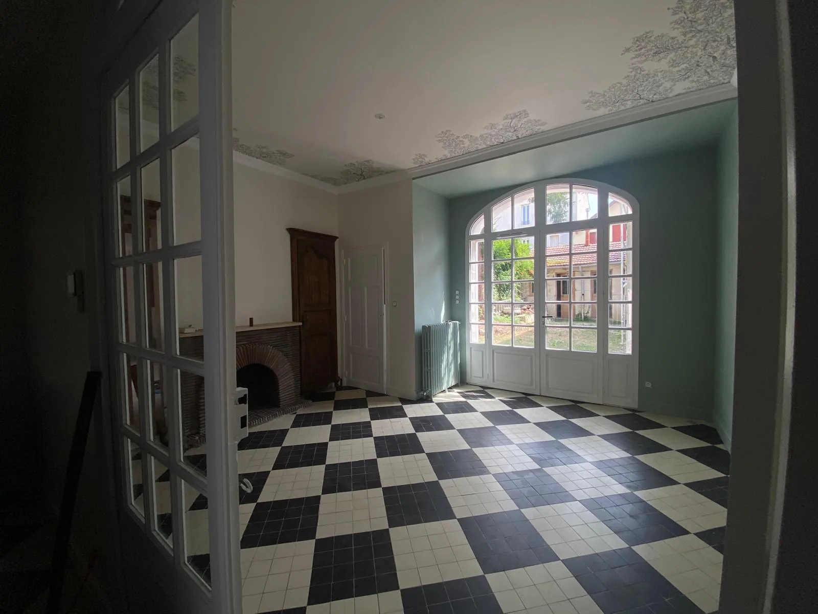 Pièce de réception rénovée en bâti ancien, carrelage damier noir et blanc et porte-fenêtre cintrée